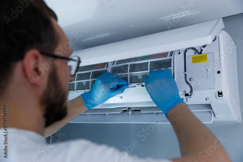 A Person Performing Maintenance on an Air Conditioning Unit with Blue Gloves and Careful Attention to Details in a Modern Indoor Setting