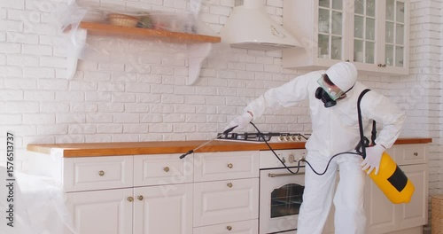 Man in protective suit and mask disinfecting kitchen during pandemic to kill bacteria. Termite pest control worker spraying and cleaning home from insects. Sanitary treatment concept