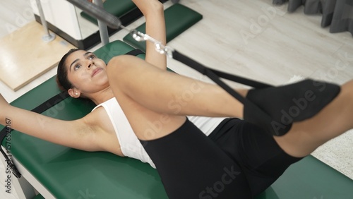 Woman performing pilates leg workout on trapeze table to improve core and leg strength at gym. Happy trainer doing supine leg extension with strap on cadillac for improving hip flexibility. Habituate.