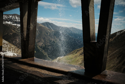 Fotografía Dramatic mountain vista seen through a concrete structure with splashing water in the foreground