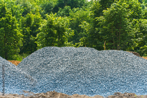A pile of gravel or small stone for construction, material for repairing the roadway or creating concrete. Gravel on the background of the forest.