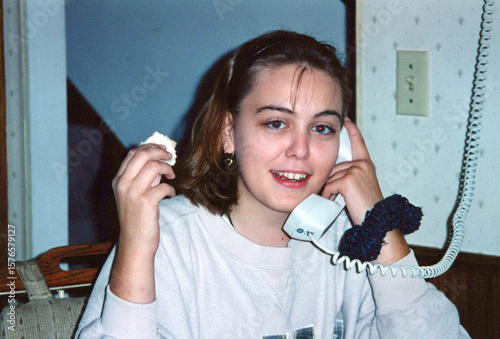 Circa 1996 - teenage girl talks on a landline phone with her friend while eating. Scrunchie on wrist, typical 90s highschooler.