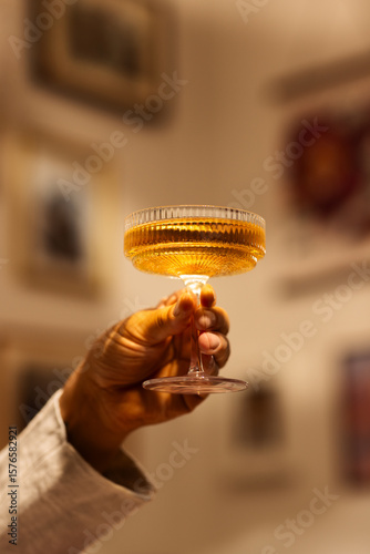 Male hand holds drink in glass  against blurry background. Concept of alcohol, drink, party, degustation, holiday. Copy space for ad.