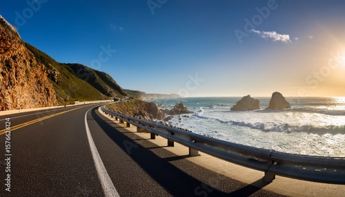 coastal highway long shadows from rocky outcrops stretching across the pavement guardrails gleaming above crashing surf road disappearing around a dramatic headland