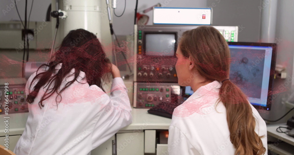 Obraz premium Two female researchers operating scanning electron microscope in research lab, with monitor data