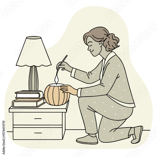 Woman in pajamas lighting a candle on a pumpkin on a nightstand with a lamp and books in the room
