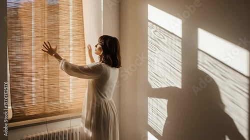 Woman adjusting bamboo window blinds in a well lit room capturing soft sunlight and shadows effect heatwave climate global change