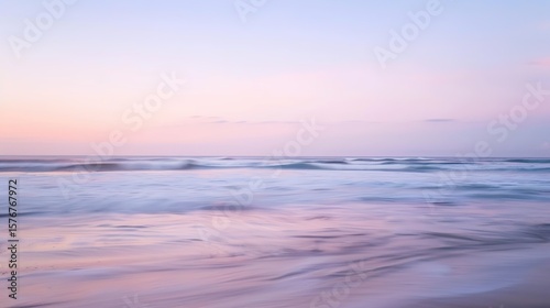 Soft pastel sunset painting the sky over a calm ocean beach  with gentle waves lapping the shore. The sky blends hues of pink  blue  and purple  while the water mirrors the serene colors  