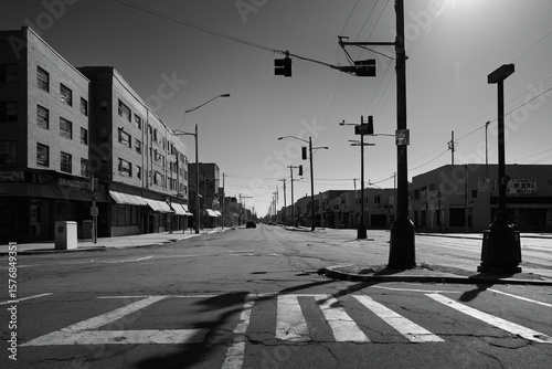 An abandoned city block in black and white with geometric shadows from lampposts falling across a wide empty intersection under a cloudless sky this image is rendered in ultra HD clarity