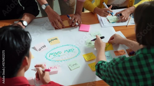 Top view of business team in casual cloth hand writing idea on sticky notes. Closeup of diverse people brainstorming marketing idea while sticking colorful sticky notes on mind mapping. Convocation.