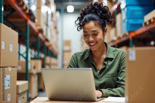 Female Entrepreneur in a Warehouse Office Surrounded by Colorful Shipping Boxes, Hard at Work on Laptop