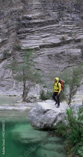 Long shot of a mexican man in yellow stays over a rock by a water pool