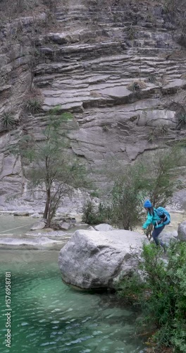 Long shot of a mexican woman that climbs a rock over a pond of blue water and looks away