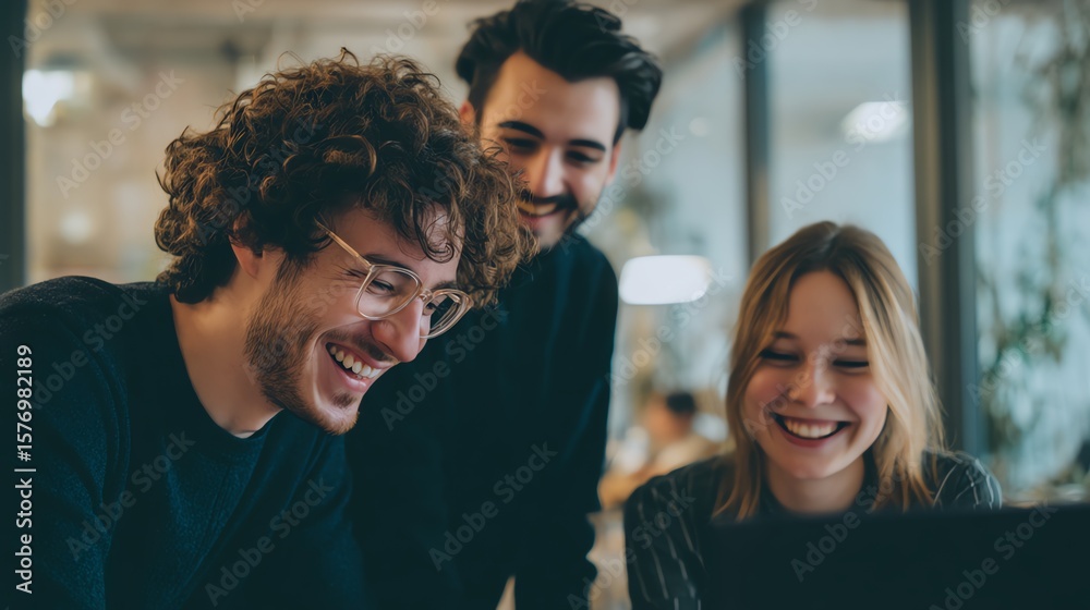 Three young professionals collaborate happily around a laptop in a modern office setting. Three young professionals collaborate happily around a laptop in a modern office setting.