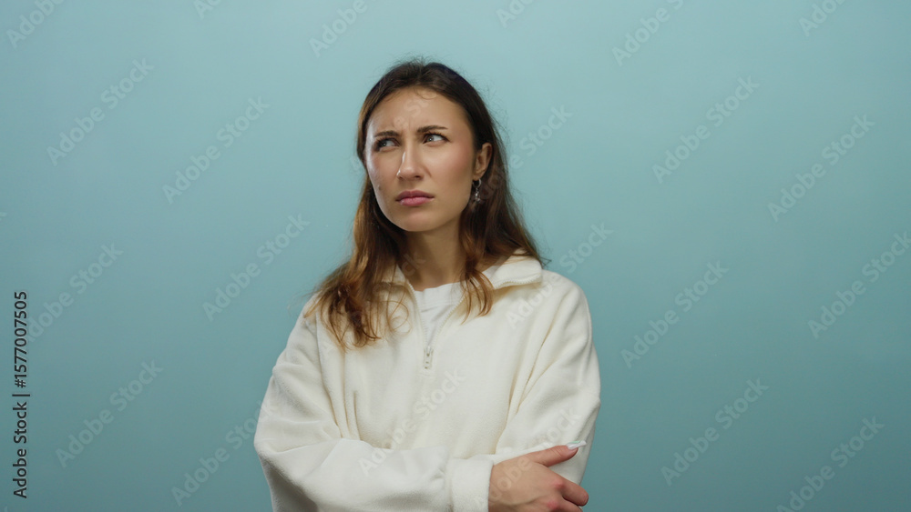 Woman with brown hair crossing arms over isolated blue background, showing a thoughtful expression, wearing a white sweater, evoking introspection in a serene setting. Woman with brown hair crossing arms over isolated blue background, showing a thoughtful expression, wearing a white sweater, evoking introspection in a serene setting.