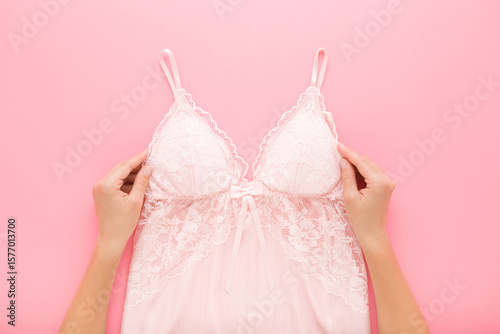 Konstfotografi Young adult woman hands holding and showing new silk lace nightgown on light pink table background