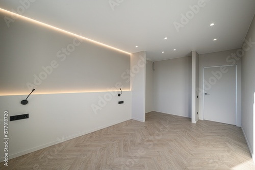 Photography modern room featuring a herringbone wood floor, beige walls with indirect lighting, and sleek black sconces and outlets