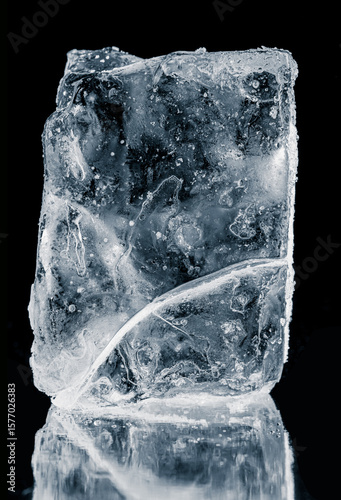 Textured natural ice block with cracks, on a black background with reflection. A melting piece of ice.