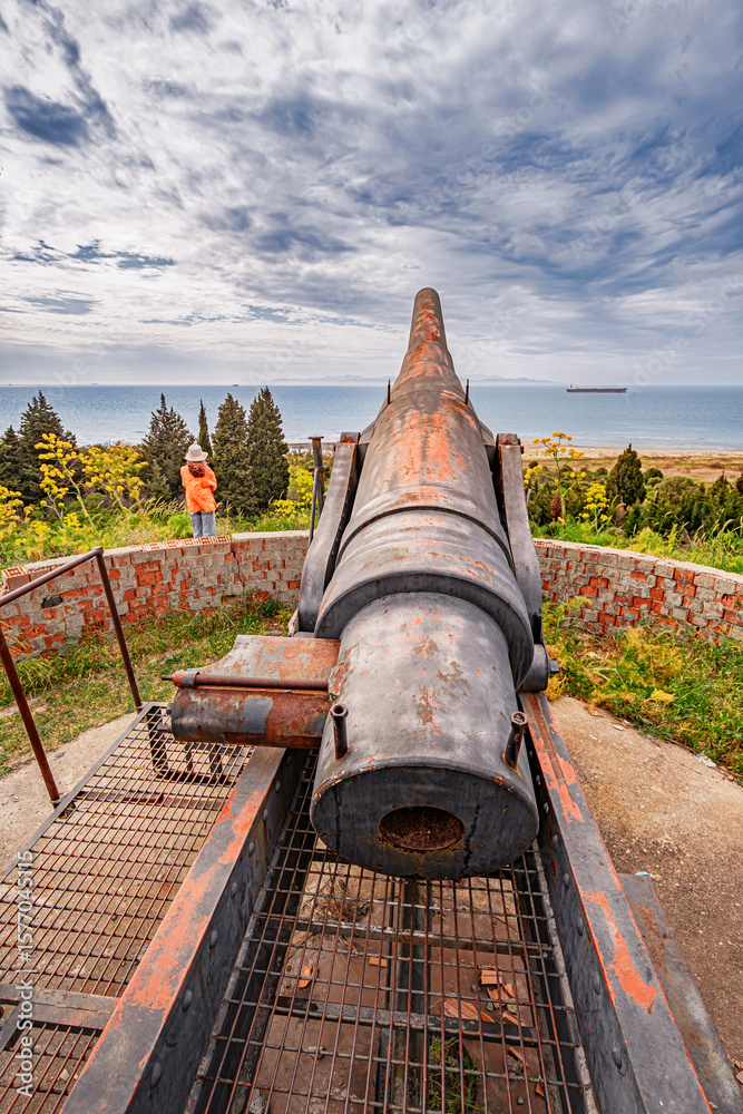 Tourist pointing at an old Turkish military cannon overlooking the Dardanelles Strait in Turkey, exploring national heritage and historical defenses Tourist pointing at an old Turkish military cannon overlooking the Dardanelles Strait in Turkey, exploring national heritage and historical defenses