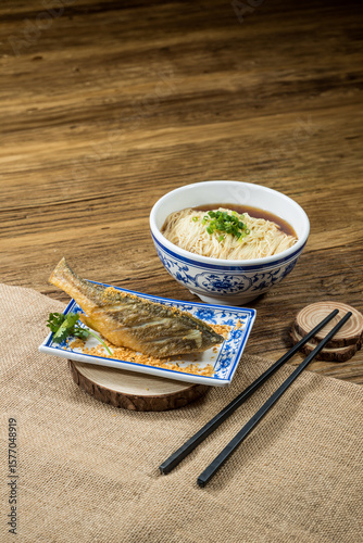 A Chinese style crispy yellow croaker served with plain noodles set against a wooden background