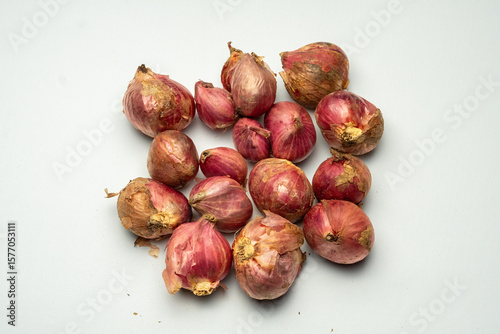 Sixteen whole unpeeled shallots are neatly arranged on a clean white background, showcasing their natural red skin, perfect for cooking, food photography, or kitchen decoration.