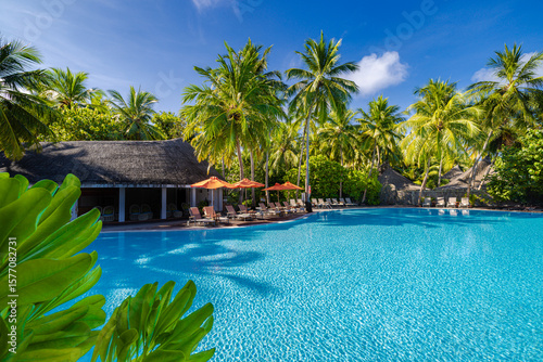 Stunning sunny tropical resort in Maldives swimming pool, palm leaves, loungers umbrella under blue sky and clouds peaceful relaxing summer vacation luxury travel scene. Picturesque tourism background