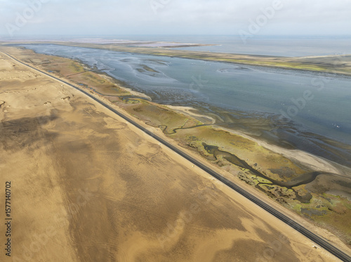 Aerial view of a straight road cuts through the arid landscape alongside the brackish river leading to the sea, Windhoek, Khomas Region, Namibia.