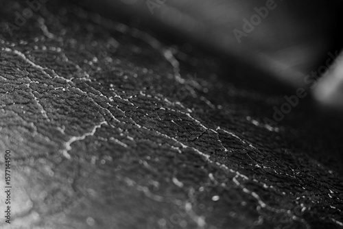 Monochrome image, worned, cracked deteriorated leather seat on car interior close up hot.