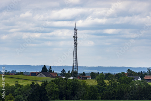 Aerial view of a towering communications tower rising above the green fields and scattered rooftops under a cloudy sky, Southwest Germany, Baden-WÃ¼rttemberg, Germany.