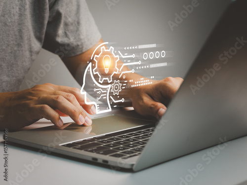 Person typing on laptop keyboard with digital light bulb and gear icon representing innovation and technology concept