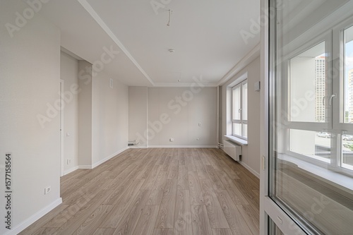 An empty, light-filled room with wood-look flooring, white walls, and large windows offering an outdoor view