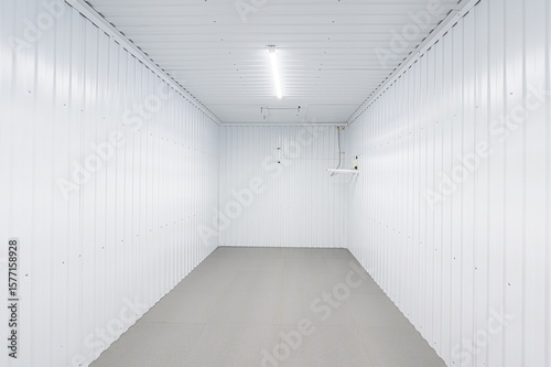 empty  clean  white storage container or room with ridged walls and a gray tile floor. A single fluorescent light illuminates the space from the ceiling