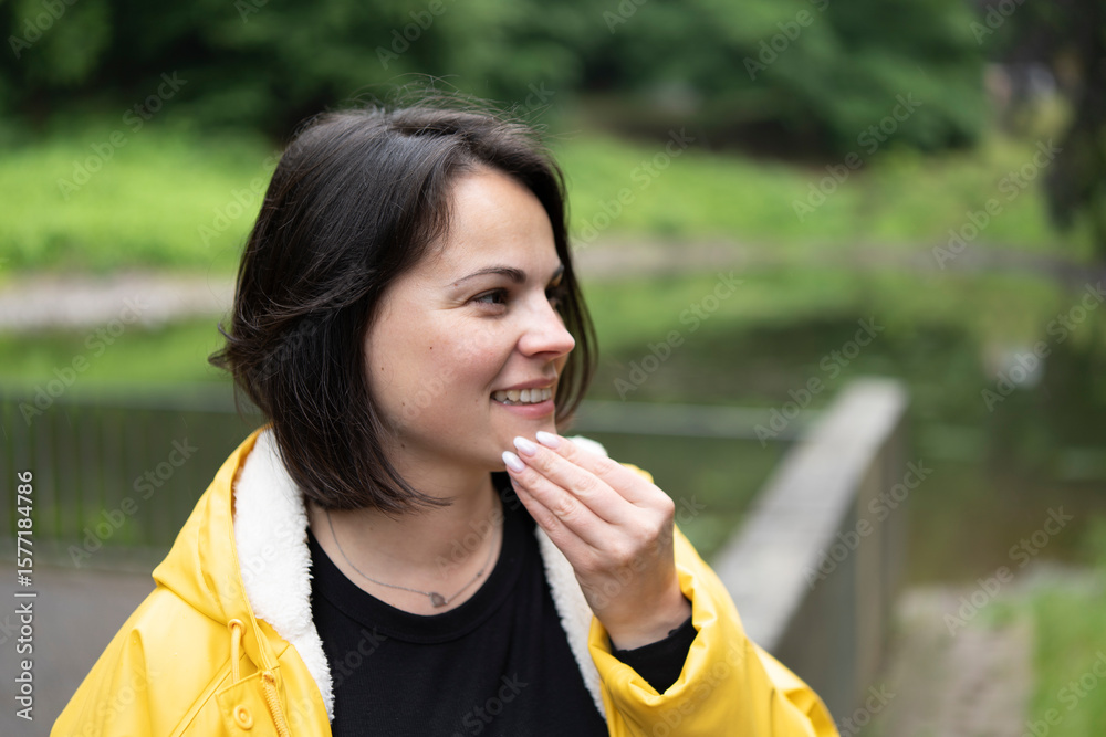 Fototapeta premium Smiling woman in a yellow raincoat close-up in the forest. Concept: joy in nature, outdoor resilience, bright mood, connection with the wild, weatherproof happiness.