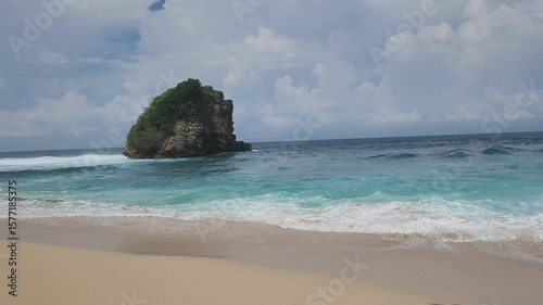 A serene tropical beach scene featuring the mesmerizing turquoise waters of the ocean gently meeting a sandy shore with foamy white waves. The vast blue sky is adorned with fluffy white clouds, sugges