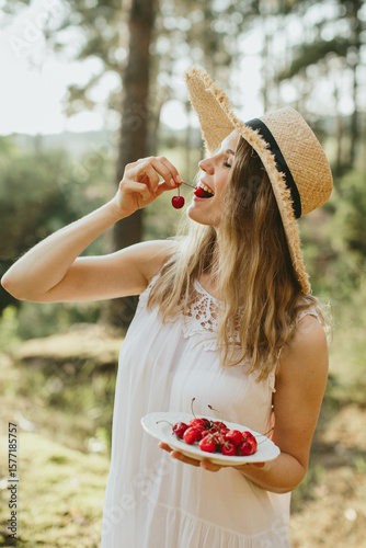 Woman eating cherries in nature holding plate and smiling