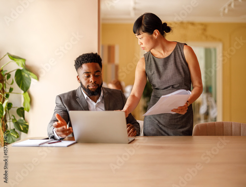 Serious financial professionals analyzing reports over laptop while working together at office desk