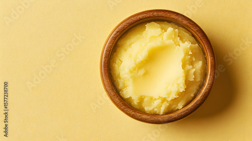 A close up shot of freshly made ghee or clarified butter in a wooden bowl against a simple yellow background