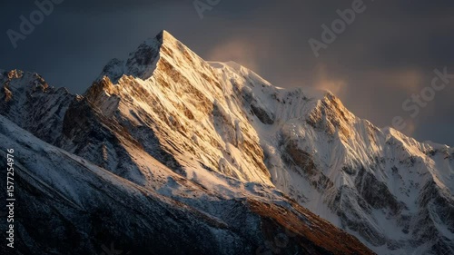 Snowy Mountain Peak Bathed in Golden Light During Dusk Against Dramatic Sky