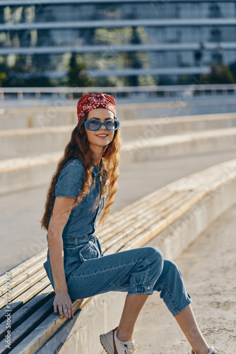 Lifestyle woman in modern boho-western denim street style wearing vintage sunglasses and a red bandana, captured with warm film color tones and natural outdoor lighting.