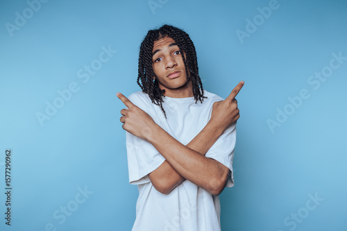young man gestures while pointing in different directions, embodying a sense of indecision on blue background
