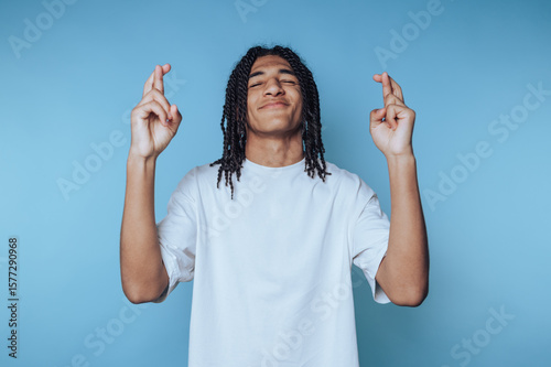 фотографія young man with dreadlocks stands with fingers crossed, displaying hope and antic