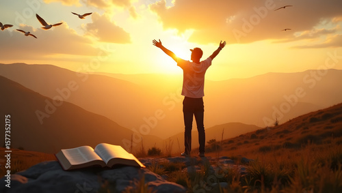 Man with arms raised towards the sunlight with a bible on the rock in the mountains