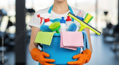 White woman wearing orange gloves carries a blue bucket filled with cleaning supplies closely
