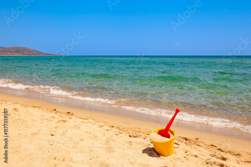 Colorful beach toys on sand near calm sea during sunny summer day