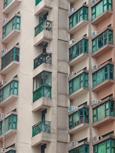 In this bustling area of Hong Kong, numerous residential apartments display distinct balcony styles, with many units featuring colorful curtains and air conditioning units, typical of urban living.