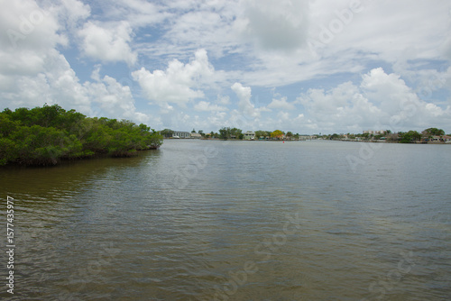 Serene Waterfront Scene of Boats, Calm Water, and Distant Coastal Residences. Tranquil waterfront view featuring serene water, recreational boats in motion, and a coastal residential background under 