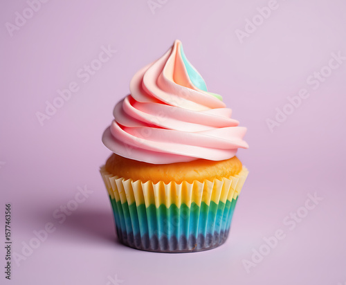 A delectable cupcake features a swirled frosting in pastel pink with a rainbow wrapper, creating a joyful and colorful treat against a soft lavender background for celebrations.