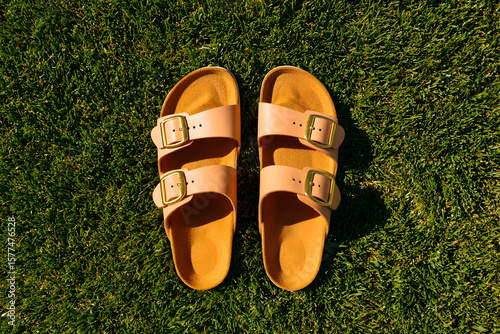 Stylish sandals sit on lush green grass, soaking up the warm sunlight of a sunny afternoon in summer