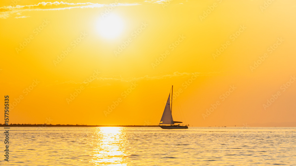 Fototapeta premium Sailing ship on Lake Constance before sunset, the sun illuminates the lake and conjures up intense colors on the water and the sky, black silhouettes against a bright backlight, holiday cruise
