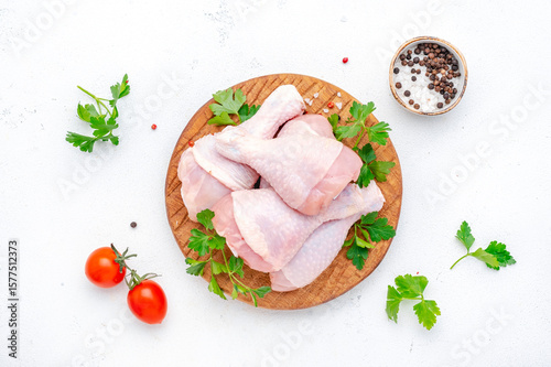 Raw chicken legs or drumsticks on wooden board with pepper, salt and parsley, top view